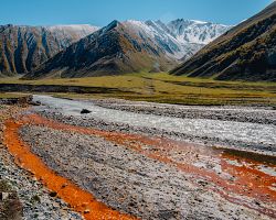 Setkání modré a oranžové železité řeky v soutěsce Truso s výhledem na vrcholky Kavkazu u Kazbegi