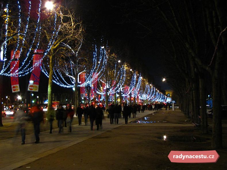 Osvětlenou Champs-Éllysées prochází davy lidí.